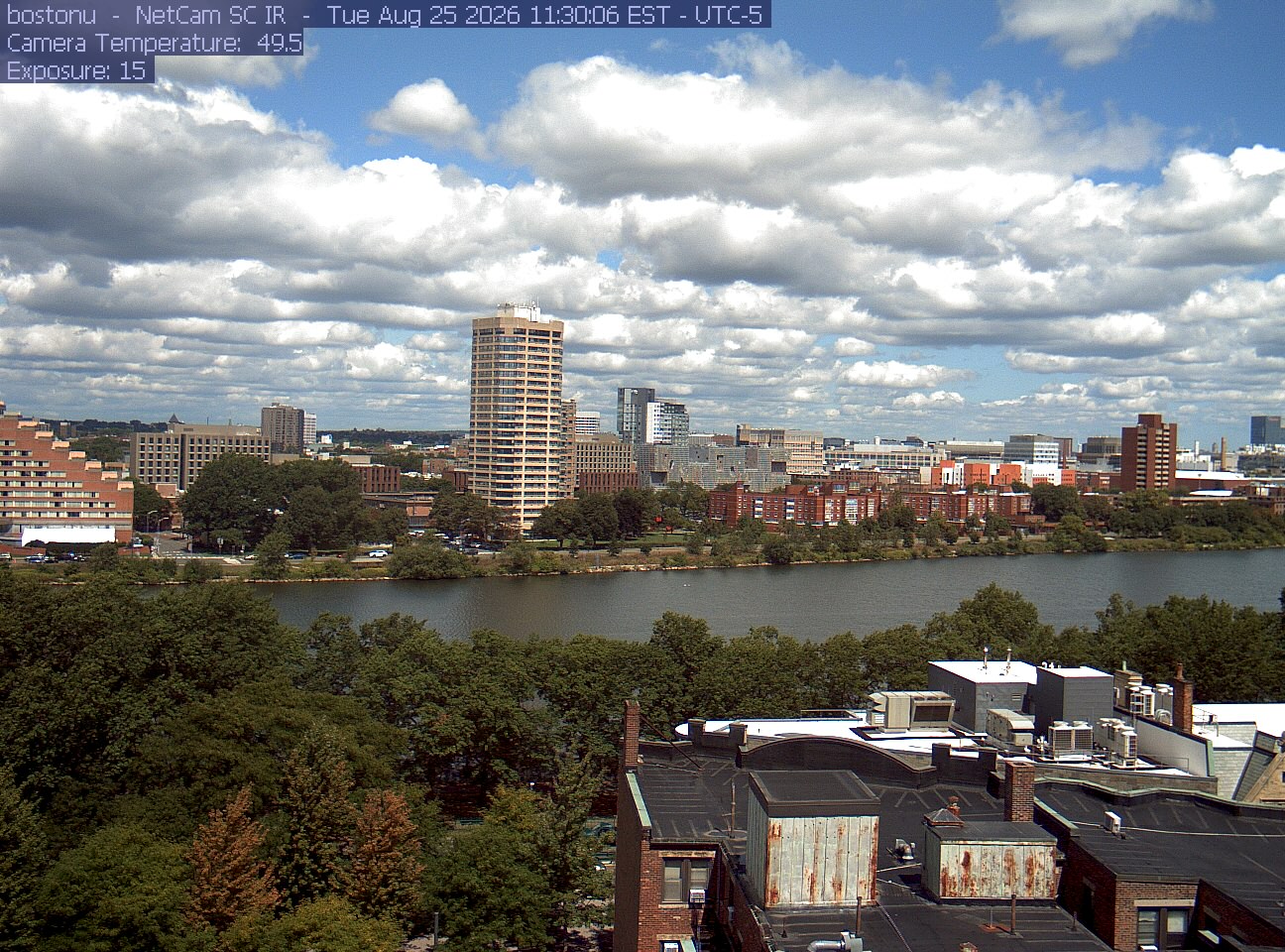 Trees line the river below the city skyline, with a roof edge in the foreground.