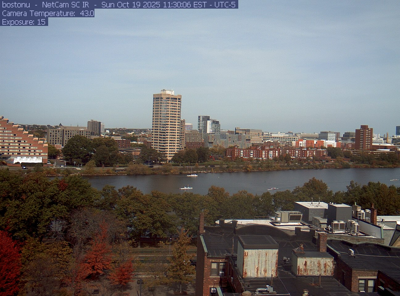 Trees line the river below the city skyline, with a roof edge in the foreground.