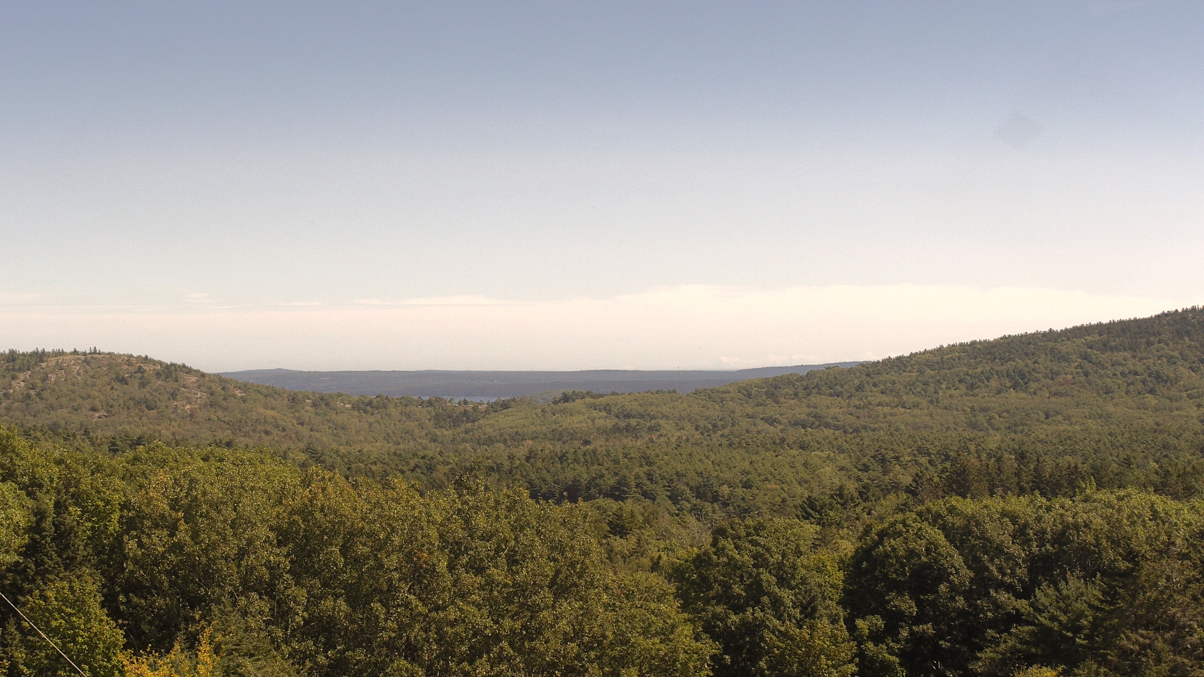 A wooded valley opens toward distant water, seen from McFarland Hill.