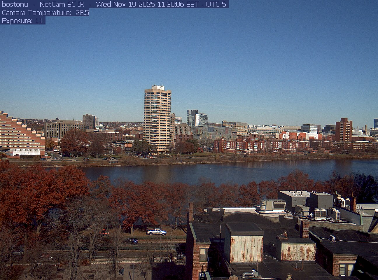 Trees line the river below the city skyline, with a roof edge in the foreground.