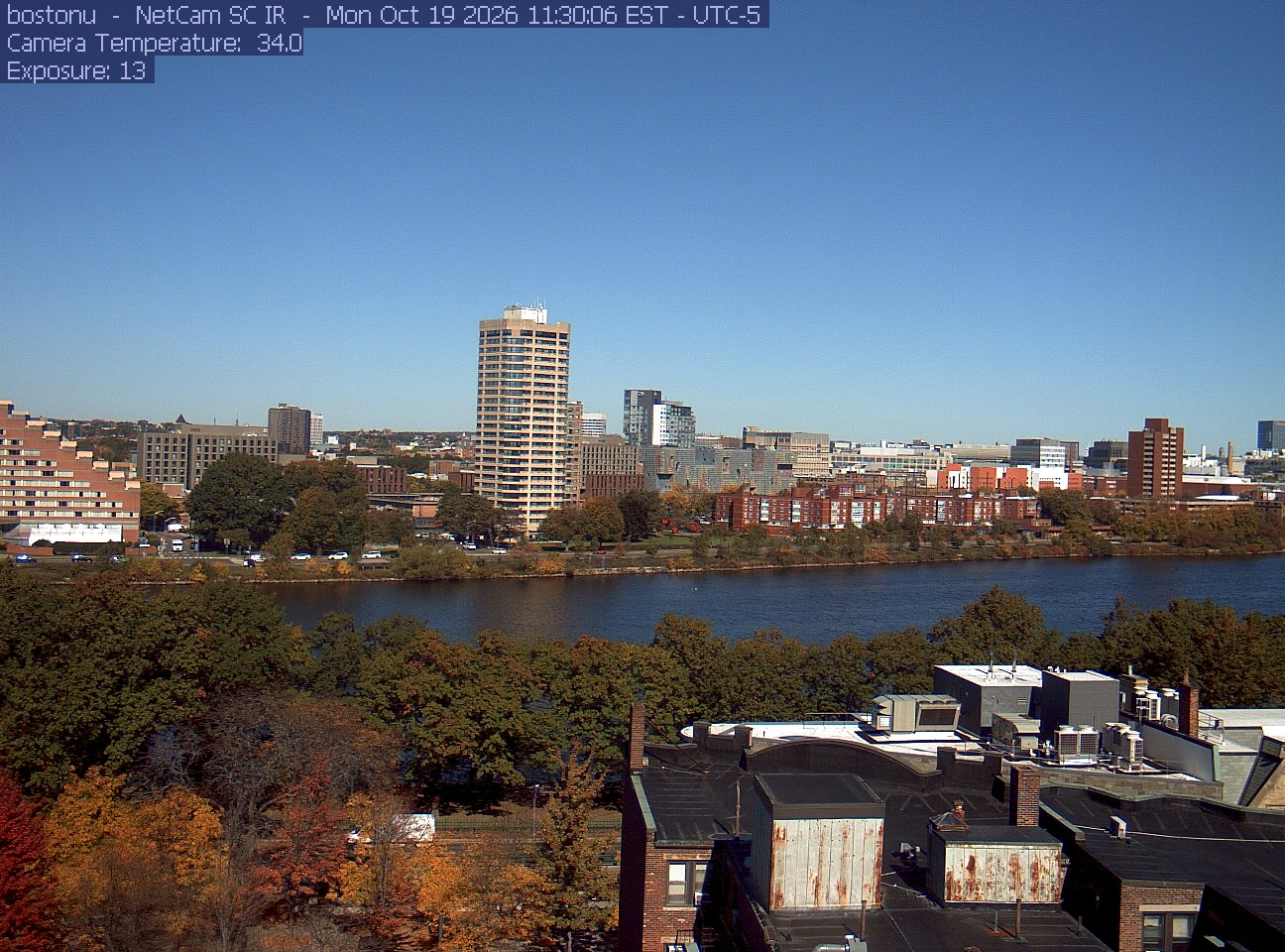 Trees line the river below the city skyline, with a roof edge in the foreground.