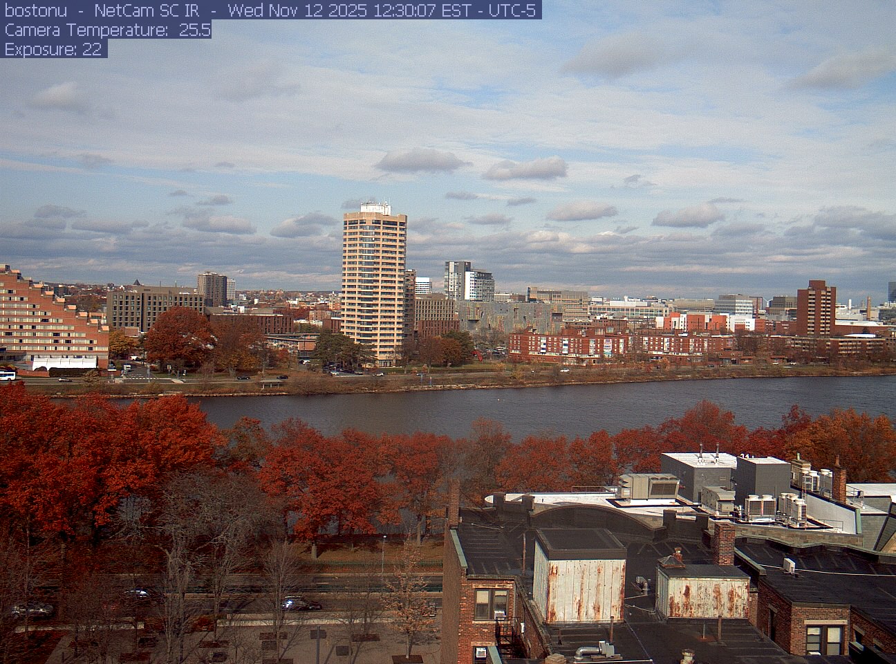 Trees line the river below the city skyline, with a roof edge in the foreground.