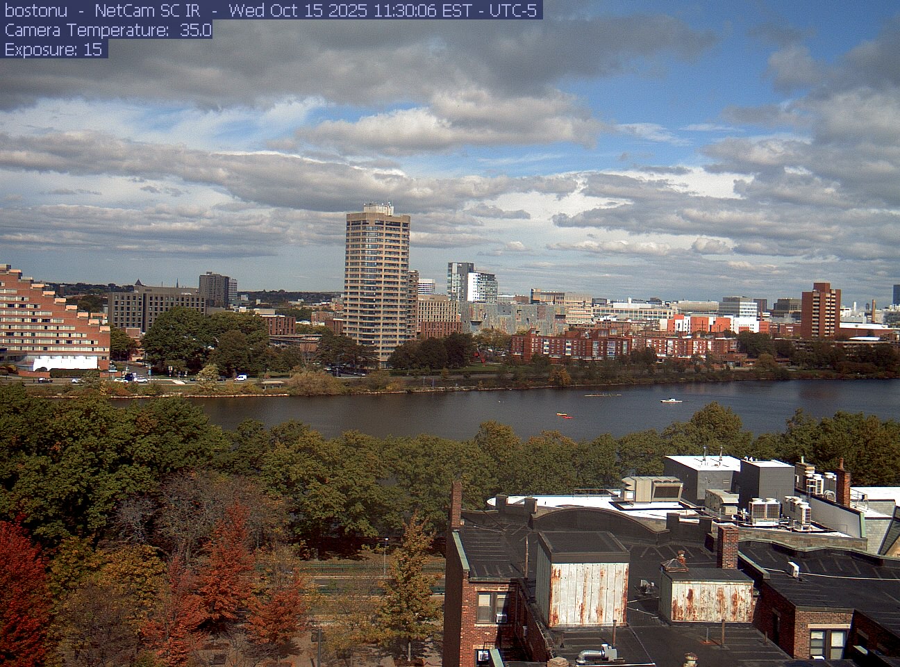 Trees line the river below the city skyline, with a roof edge in the foreground.