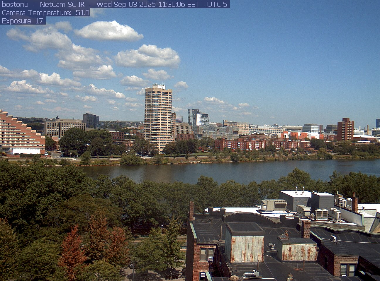 Trees line the river below the city skyline, with a roof edge in the foreground.
