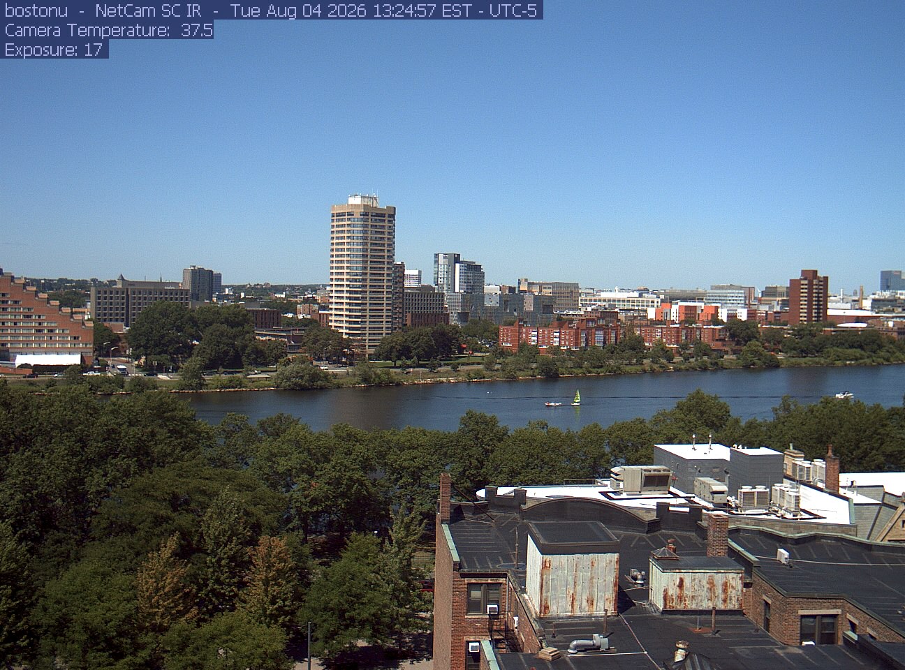 Trees line the river below the city skyline, with a roof edge in the foreground.