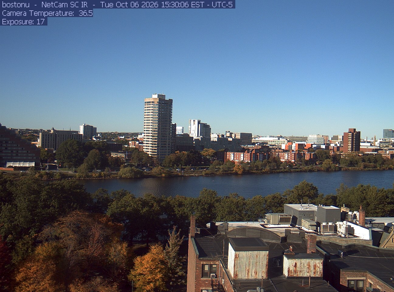 Trees line the river below the city skyline, with a roof edge in the foreground.