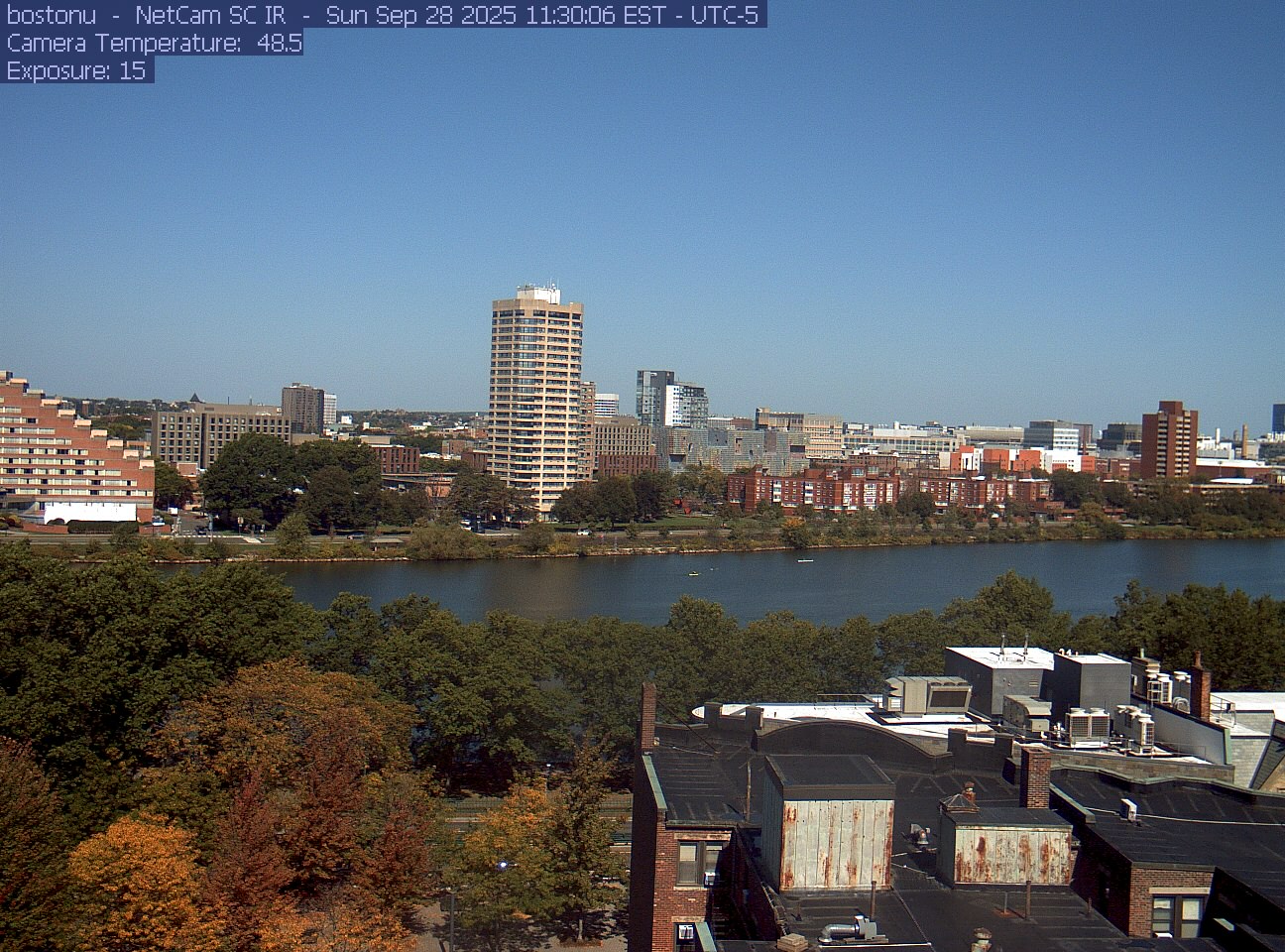 Trees line the river below the city skyline, with a roof edge in the foreground.