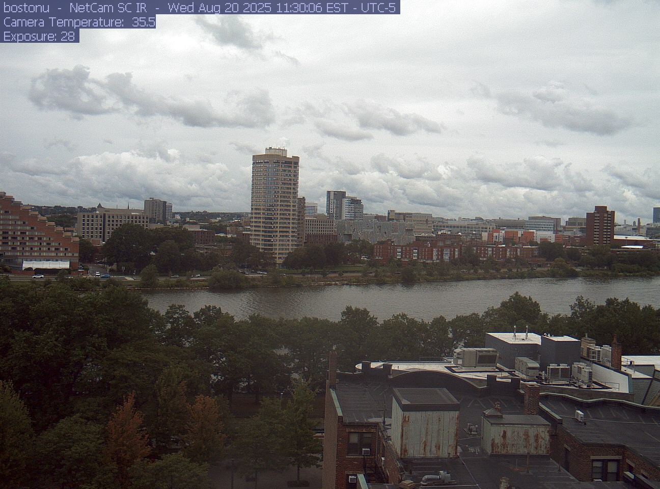 Trees line the river below the city skyline, with a roof edge in the foreground.
