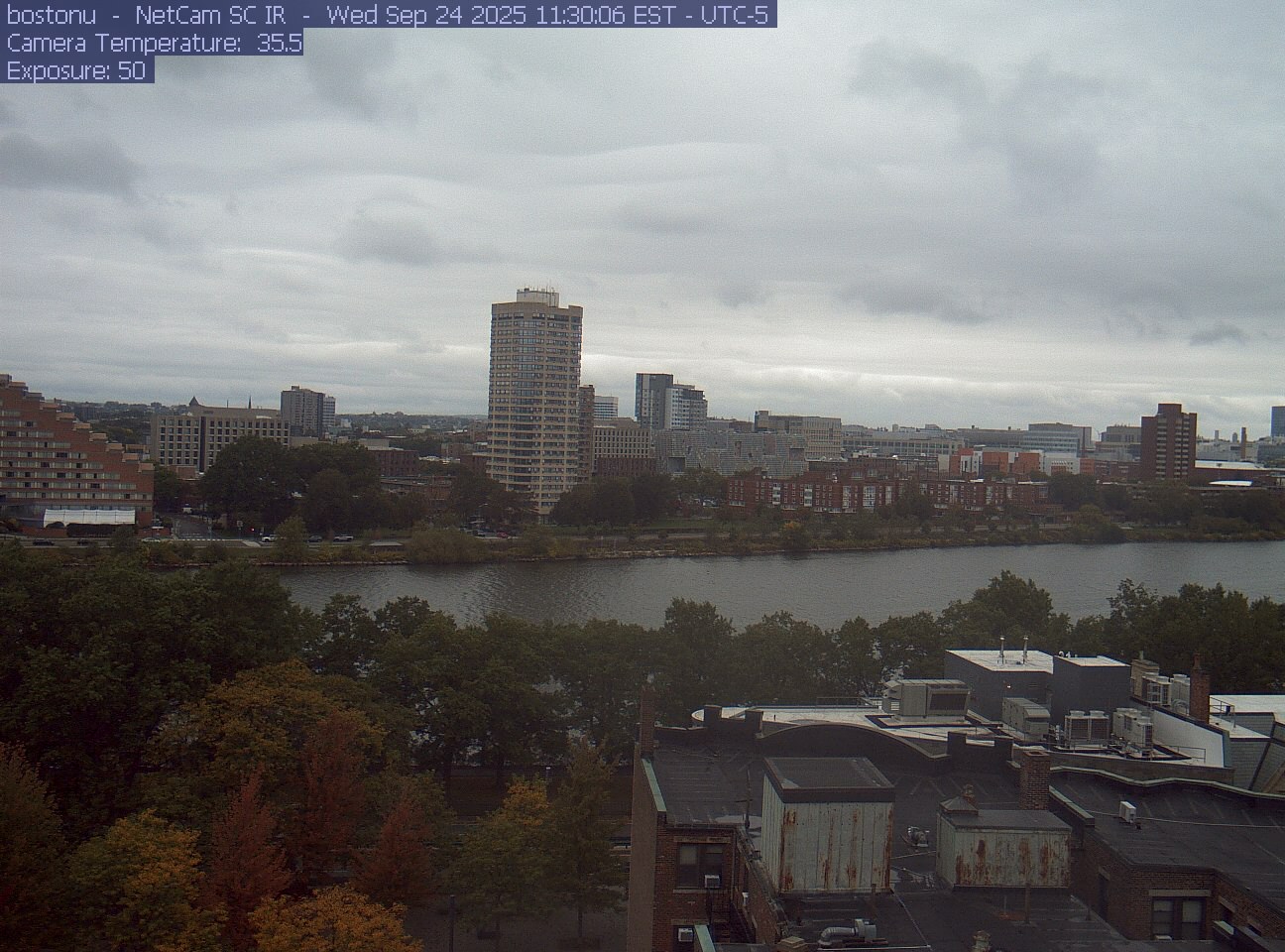 Trees line the river below the city skyline, with a roof edge in the foreground.