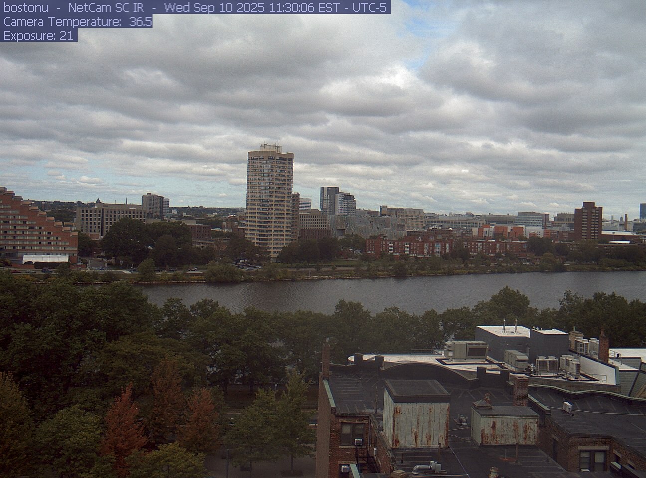 Trees line the river below the city skyline, with a roof edge in the foreground.