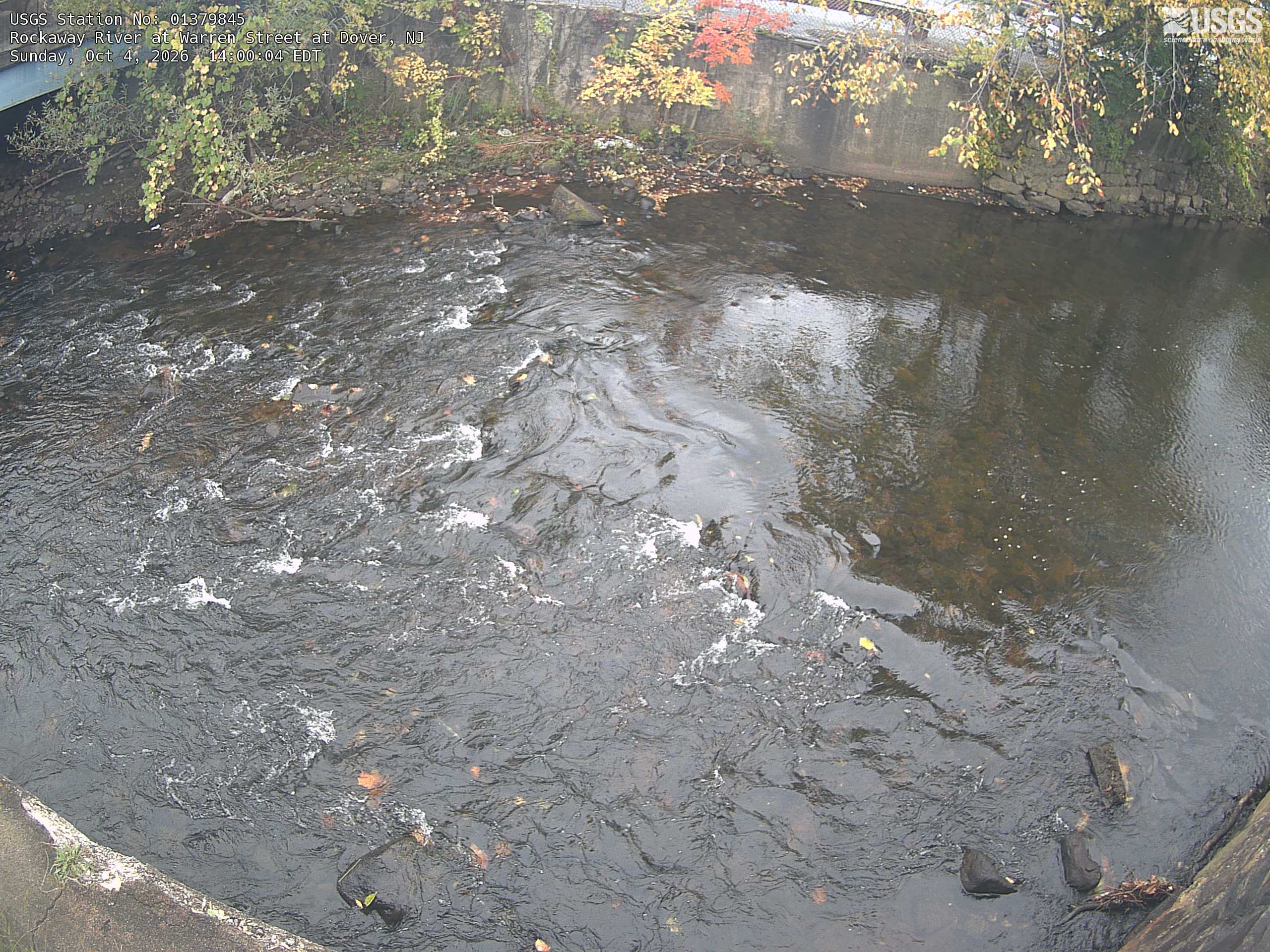 The view points mainly down at flowing water and a retaining wall.