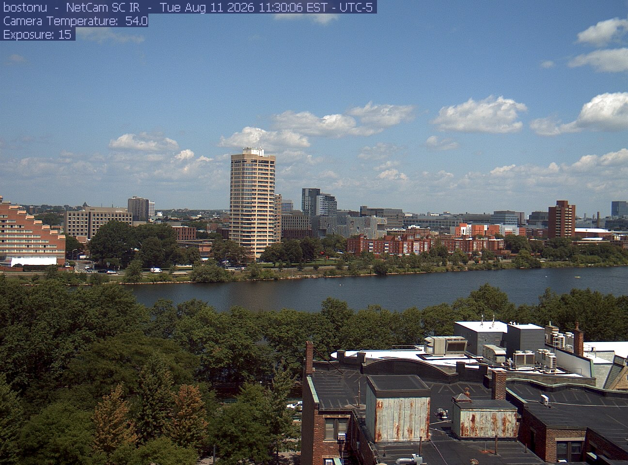 Trees line the river below the city skyline, with a roof edge in the foreground.