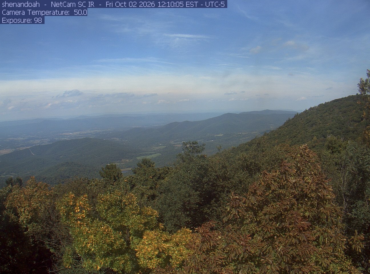 A wooded mountainside opens across a broad valley and distant blue ridges.