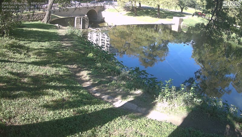 A still pool on Turtle Creek below a stone bridge, with lawns and spreading trees along the water.
