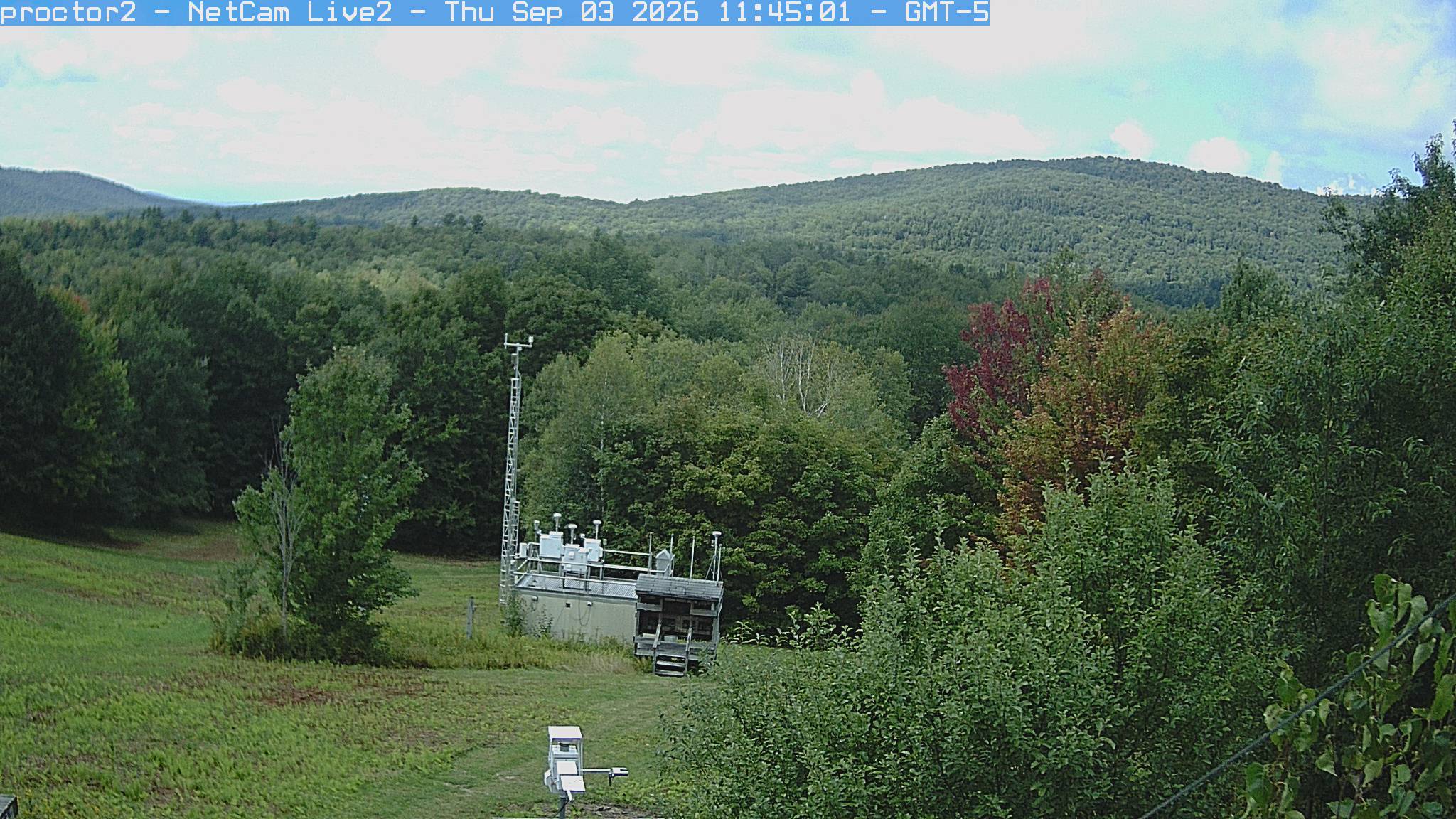 Wooded hills rise beyond an open foreground with research instruments.
