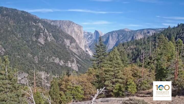 El Capitan and, far beyond, Half Dome above Yosemite Valley, with black oaks and pines in the near woods.