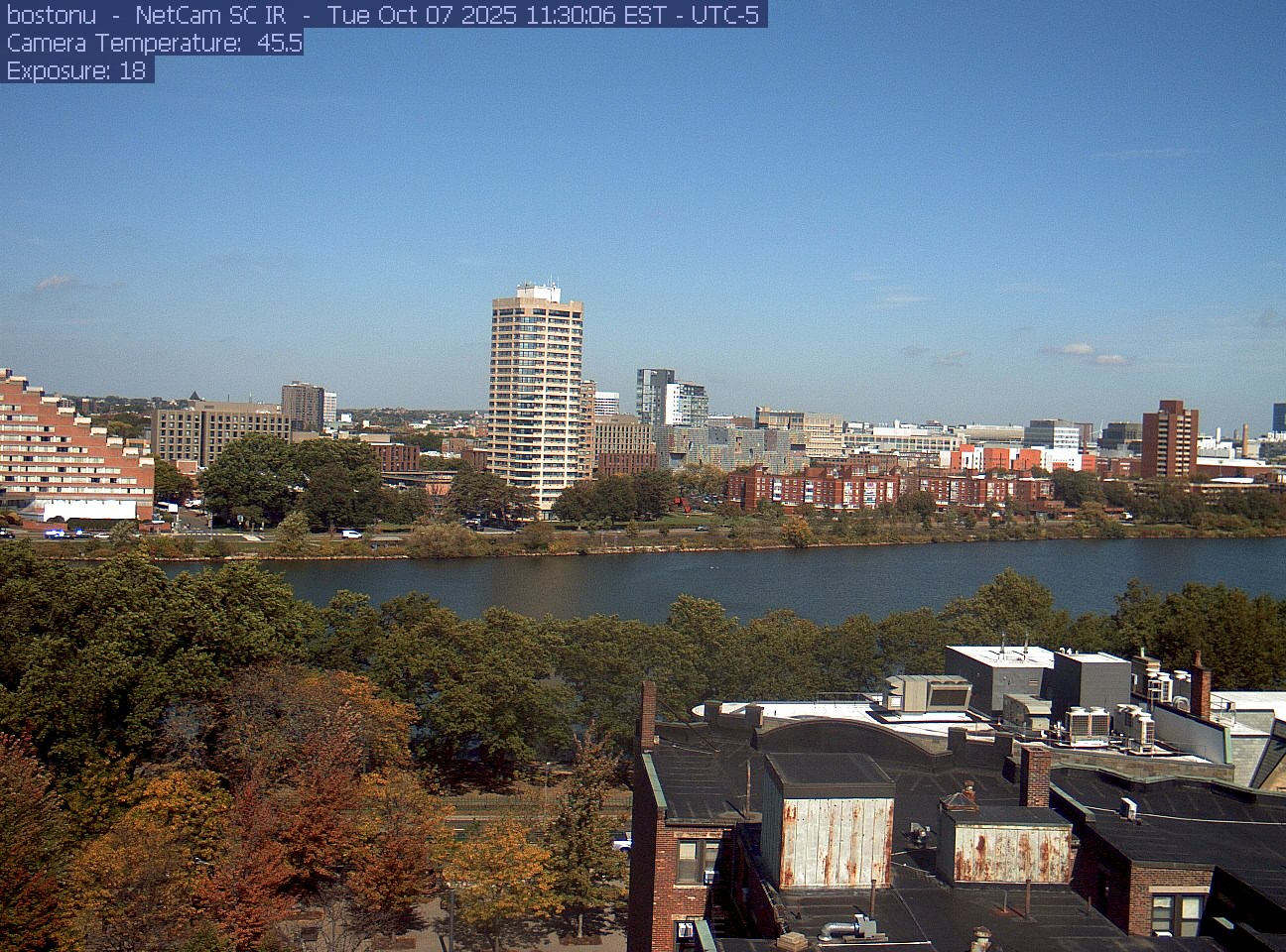 Trees line the river below the city skyline, with a roof edge in the foreground.