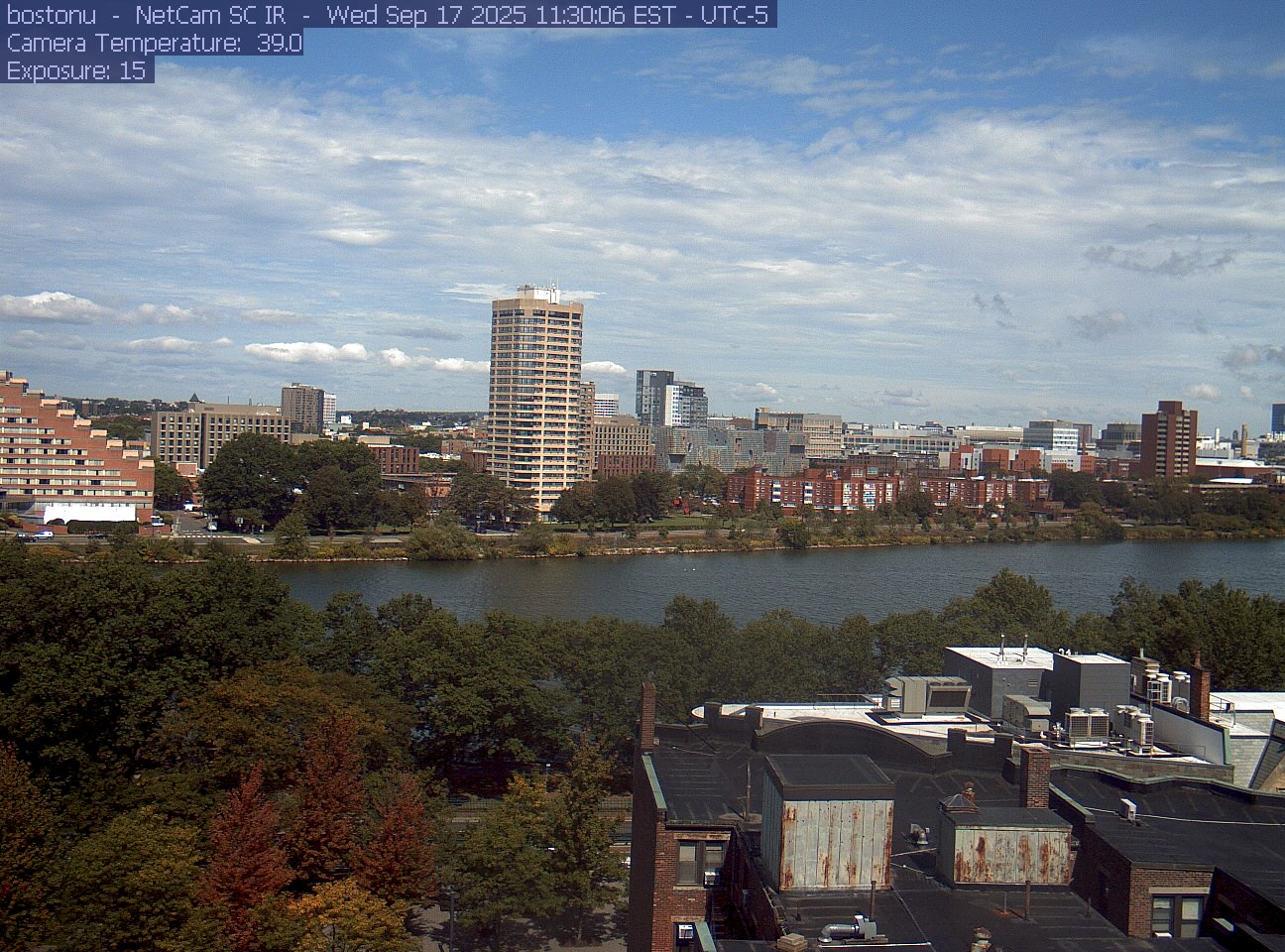 Trees line the river below the city skyline, with a roof edge in the foreground.
